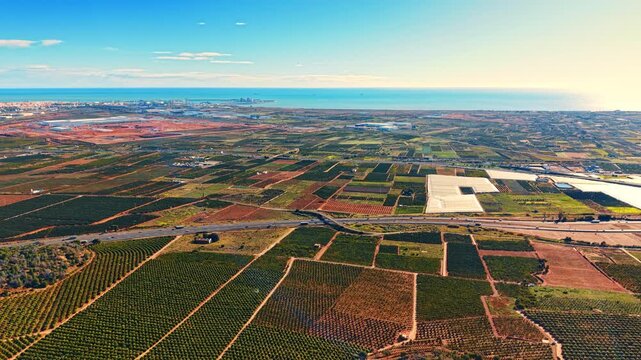 Wide angle aerial overview of agricultural landscape near sea. High view of regular grid agricultural plots, greenhouses, and an expressway adjacent to the coast.