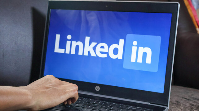 A persons hand on a laptop keyboard with the linkedin logo on the screen