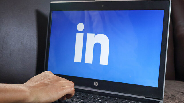 A persons hand on a laptop keyboard with the linkedin logo on the screen, displaying a blue background