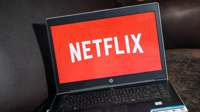 A black hp laptop with netflix on the screen sitting on a brown surface