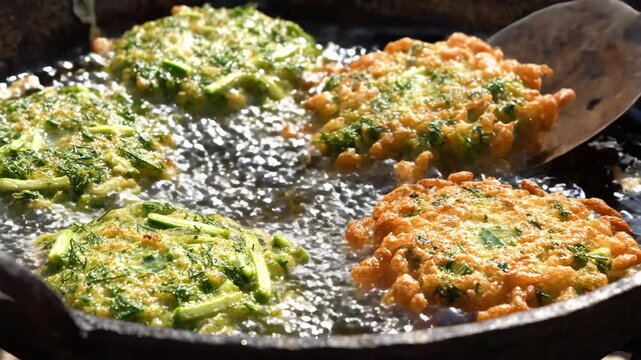 Traditional Greek herb fritters frying in hot bubbling oil inside a rustic pan