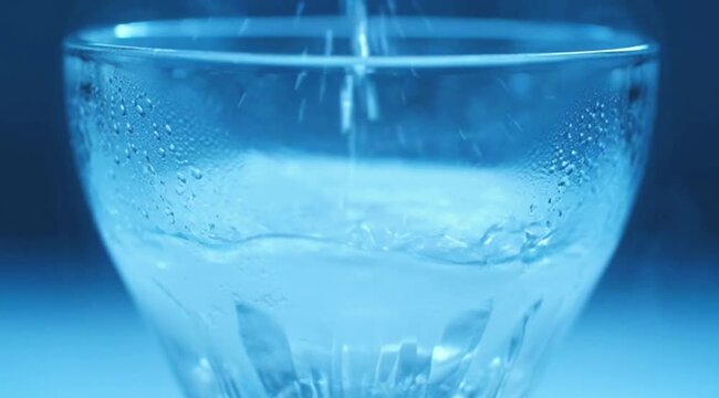 Glass of cold water with ice being poured into a transparent glass with fresh splash and bubbles on white isolated background