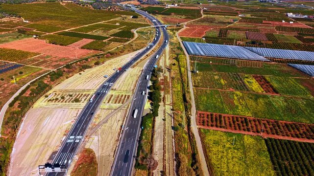 Countryside road through fields. A highway runs through green fields and farms. Vehicles travel along the road while the land stretches in the distance.