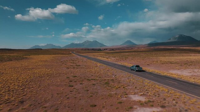 Aerial view of a car traveling through the vast landscapes of northern Chile. Desert plains and volcanic mountains stretch across the horizon.