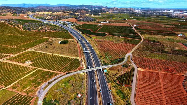 Overpass bridge over highway running through farmland. Elevated view of highway with bridge surrounded by geometric orange tree plantations and red soil.