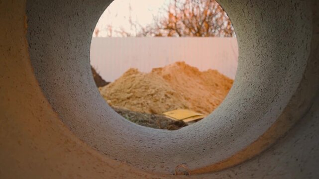 View through concrete sewer pipe ring at sand pile on construction site
