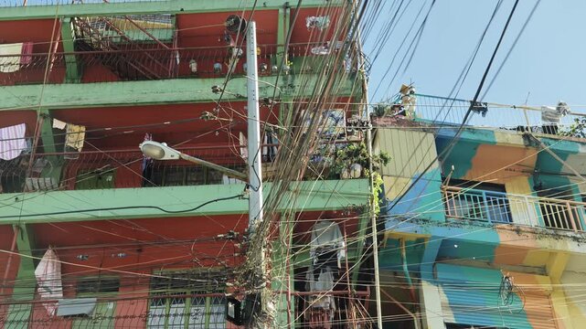 Vivid hillside apartments contrast tangled utility wires beneath sunny blue sky