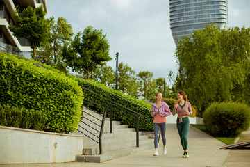 Obraz premium Friends jogging in a park near modern buildings on a sunny day