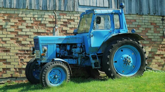 Side view of blue MTZ-80 tractor beside rustic farm building in countryside