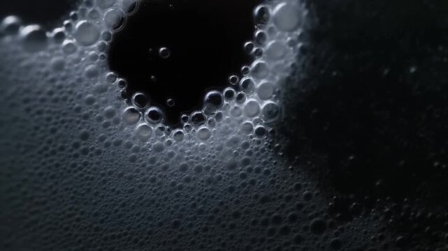 Macro slow motion tracking shot of soap bubbles forming along dark liquid surface on tabletop in studio close up