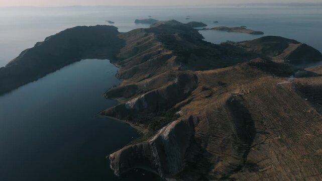 Drone view of a remote island on Lake Titicaca during sunset. Andean landscapes, traditional villages and dramatic shorelines overlook the vast lake.