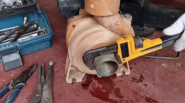 Close Up Of Plumber Tightening A Brass Pipe Coupling To Water Pump Casing Using A Large Pipe Wrench