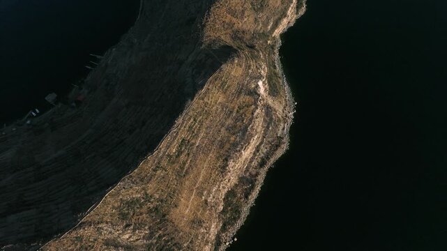 Drone view of a remote island on Lake Titicaca during sunset. Andean landscapes, traditional villages and dramatic shorelines overlook the vast lake.