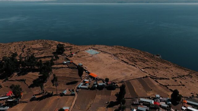 Drone view of young people playing soccer on a hillside field on Isla del Sol, with Lake Titicaca and the Bolivian Andes in the background.