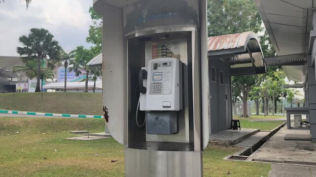 An old public telephone stands inside a vintage street booth. This classic payphone operates using metal coins for payment. Such machines are facing extinction due to the rise of modern smartphones.