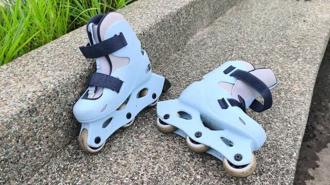 A pair of child-sized rollerblades rests on a smooth concrete bench after a fun skating session. The colorful inline skates sit quietly in the bright outdoor sunlight.