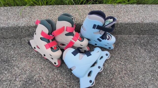 A pair of child-sized rollerblades rests on a smooth concrete bench after a fun skating session. The colorful inline skates sit quietly in the bright outdoor sunlight.