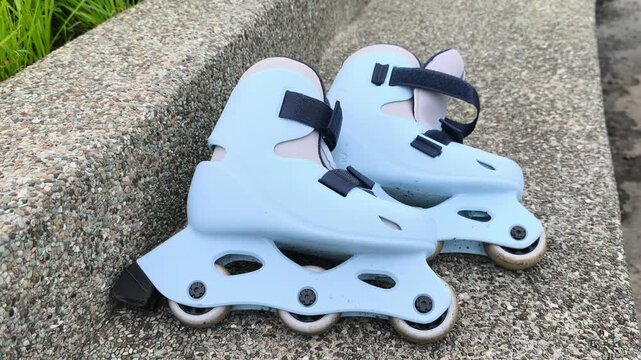 A pair of child-sized rollerblades rests on a smooth concrete bench after a fun skating session. The colorful inline skates sit quietly in the bright outdoor sunlight.