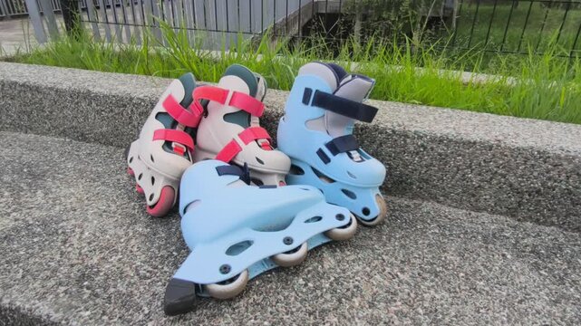 A pair of child-sized rollerblades rests on a smooth concrete bench after a fun skating session. The colorful inline skates sit quietly in the bright outdoor sunlight.