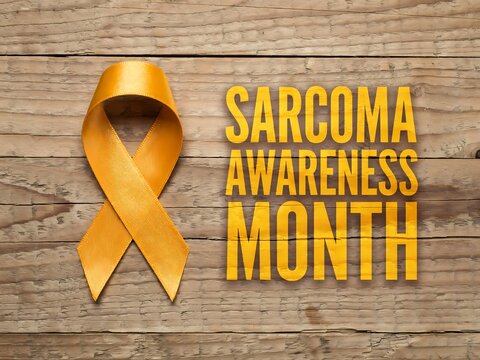 Yellow awareness ribbon on wooden background for sarcoma awareness month