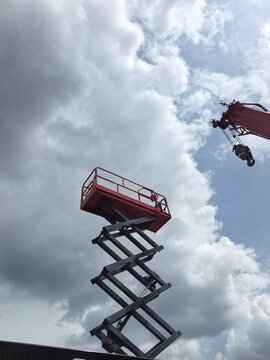Industrial scissor lift platform and crane arm against cloudy sky for construction height work