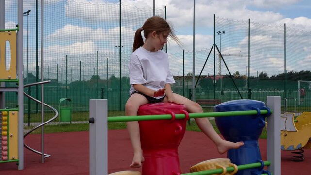 A blonde girl playing colorful playground drums on a playground and creating rhythmic sounds during outdoor play. Early childhood development through music and sensory play, focusing on creativity.