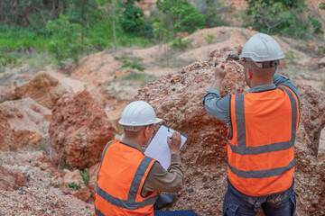 Two professional geologists team up for fieldwork, carefully examining mineral rocks and collecting soil samples to survey the mine site for geological research and industrial exploration. © reewungjunerr