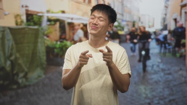 Man pointing fingers and smiling on a cobblestone street with cafe umbrellas and a passing bicycle; playful confidence.