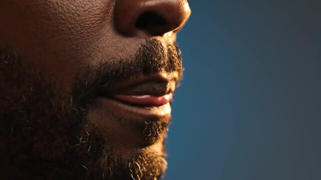 Extreme close up of a Black man's mouth and beard with warm lighting against a blue background