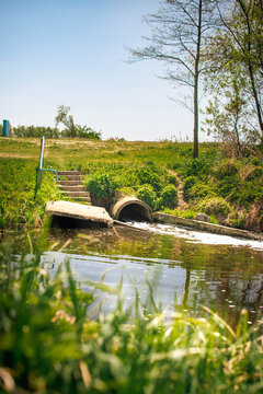 concrete drainage pipe releasing water into river with green embankment
