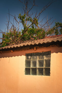weathered building facade with glass block window under corrugated roof
