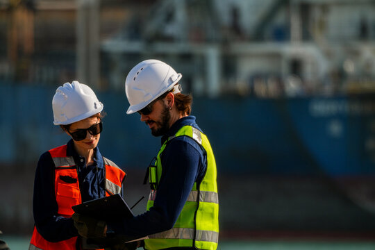 Engineering team collaborating on technical schematics and vessel maintenance plans at a bustling maritime shipyard facility during the daytime.
