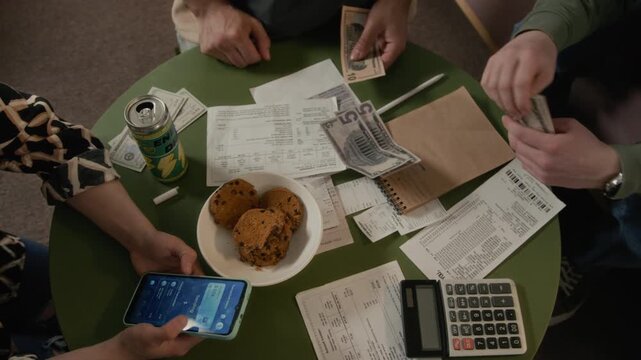 Hands of diverse young roommates calculating domestic expenses, counting small amount of cash, and writing in notebook. Commercial campaigns focusing on student debt and budgeting apps