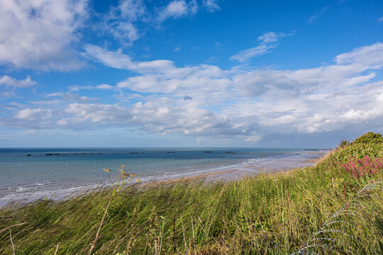 Remains of WWII Mulberry Harbour in the sea at Gold Beach in Arromanches Normandy France. Historical D-Day landing site with coastal grass.
