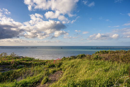 Remains of WWII Mulberry Harbour in the sea at Gold Beach in Arromanches Normandy France. Historical D-Day landing site with coastal grass.