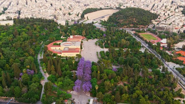 Beautiful aerial footage showing the iconic zappeion hall inside the national garden, with the panathenaic stadium and the dense cityscape of athens, greece, visible in the background