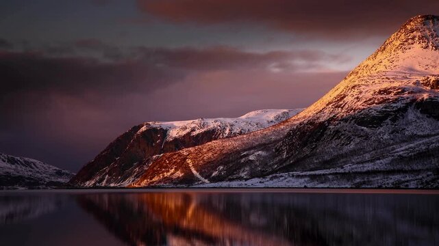 Snowy mountain range reflecting on calm lake water at sunset