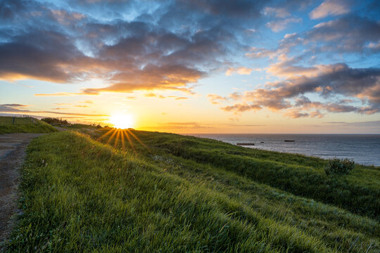 Beautiful sunrise over the Normandy coast in Arromanches France with remains of WWII Mulberry Harbour in the sea. Scenic coastal landscape.
