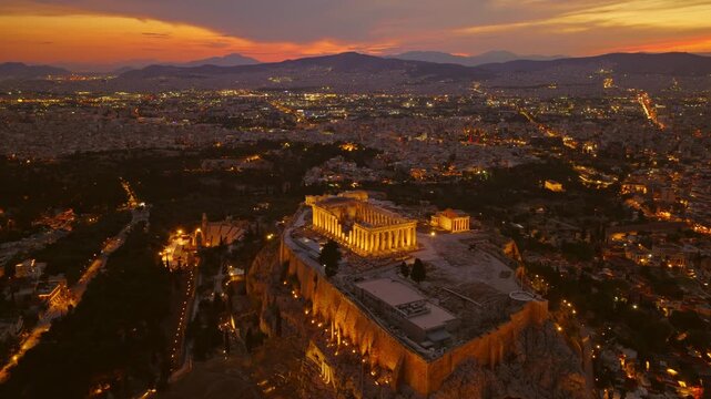 Stunning aerial footage showing the parthenon on the acropolis of athens, greece, beautifully illuminated at dusk, with the sprawling cityscape glowing in the background under a colorful sunset sky