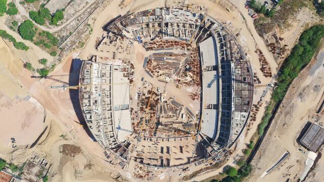 Impressive top-down aerial footage capturing the large-scale construction of a new sports stadium, showing the concrete foundations, steel framework, and heavy machinery at work on the site