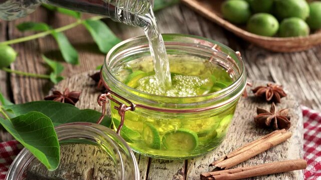 Pouring alcohol onto sliced unripe green walnuts in a glass jar - preparation of homemade nut liqueur