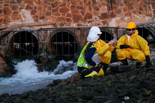 Engineering team in protective gear conducting an environmental audit, water quality sampling, and site survey at an industrial drainage outfall to ensure regulatory compliance.