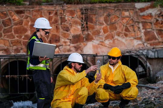Engineering team in protective gear conducting an environmental audit, water quality sampling, and site survey at an industrial drainage outfall to ensure regulatory compliance.