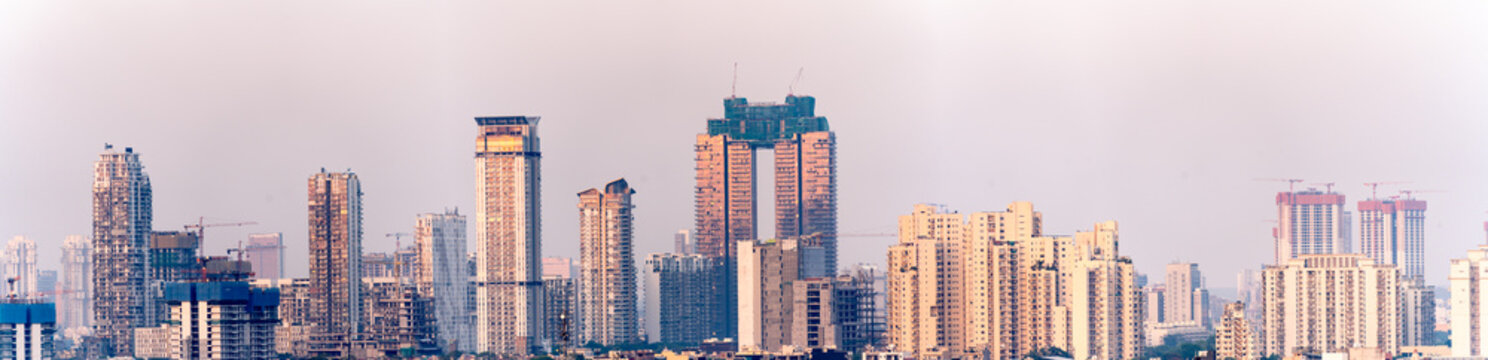 Aerial drone shot showing high rise skyscrapers under construction and completed cityscape of gurgaon delhi noida at dusk with sunlight reflected in India