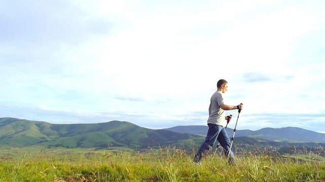 Man with trekking poles crosses mountain meadow in Zlatibor while wind moves grass. Highlights low-impact endurance training, preventive mobility maintenance, and sustainable lifelong fitness habits.