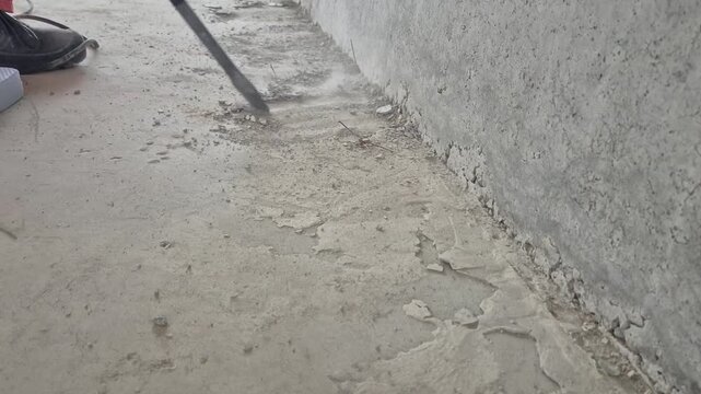 Worker using a demolition hammer on a concrete surface in front of an unfinished concrete wall at normal speed