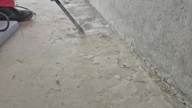 Worker using a demolition hammer on a concrete surface in front of an unfinished concrete wall in slow motion