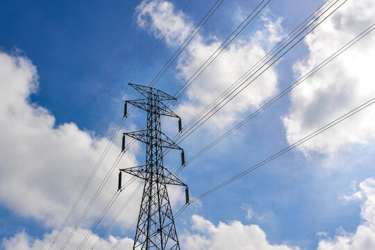 High Voltage Transmission Tower Against a Vibrant Blue Sky with Fluffy White Clouds on a Sunny Day