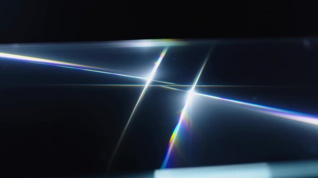 Slow motion tracking shot close up of light refraction and prism reflections crossing glass surface on dark studio tabletop with rainbow flares and high contrast highlights