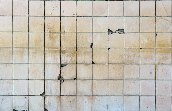 Texture of an old grunge white ceramic tile wall with cracks, stains, and dents. Vintage damaged tiled background for industrial, interior, or horror concepts.